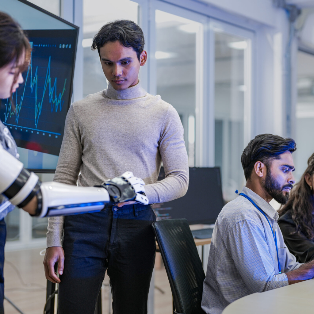 A robotics team develops a new bionic limb, inspecting the prototype while analyzing real-time performance data. A concept for digital twins, agile R&D, and mechatronics innovation.